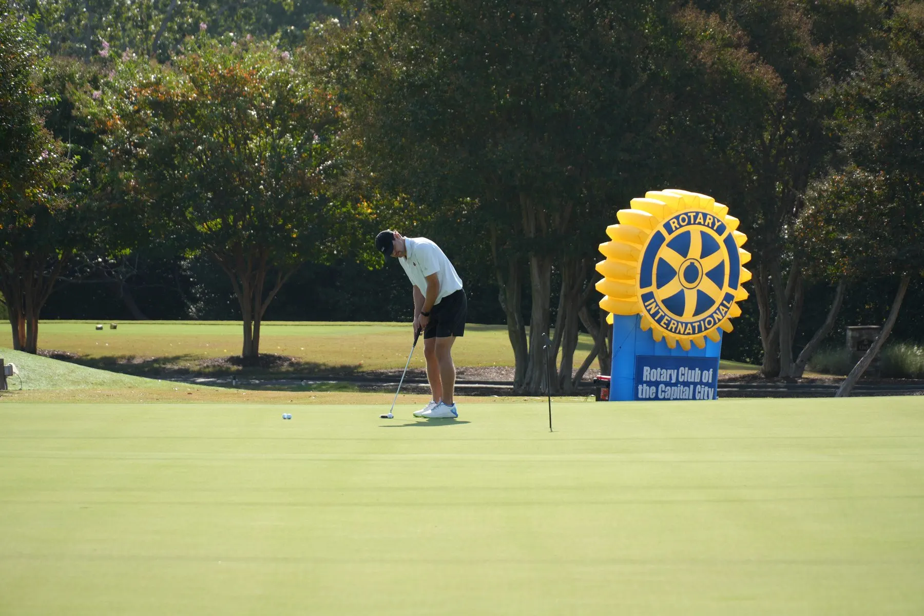 A golfer putting beside the Rotary Club of the Capital City banner at North Ridge Country Club.